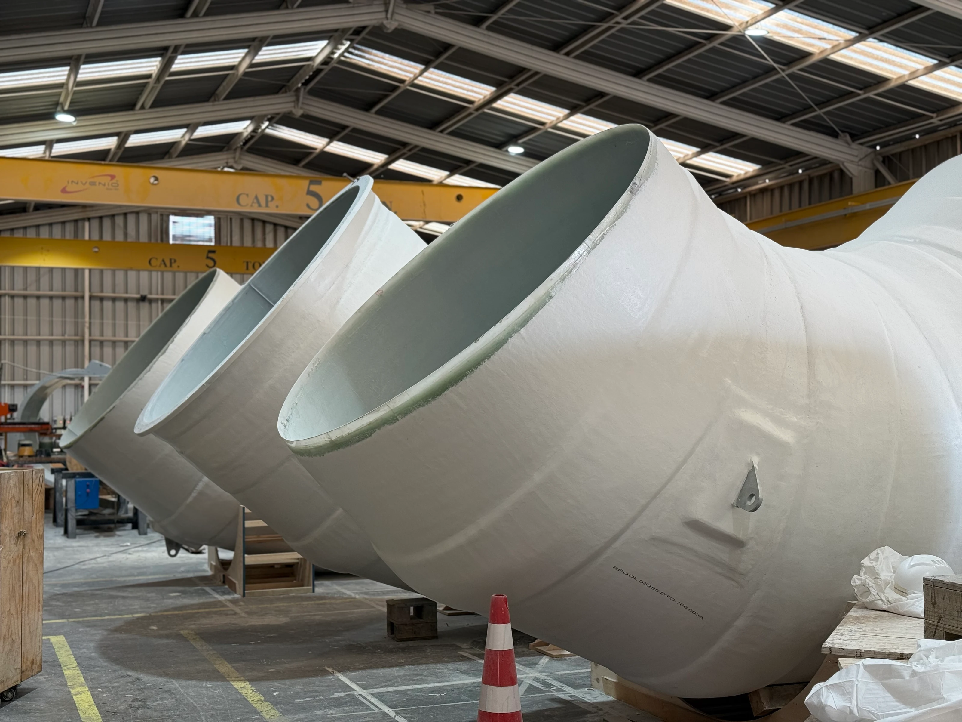 FRP piping elbows resting in the workshop, under an overhead crane.