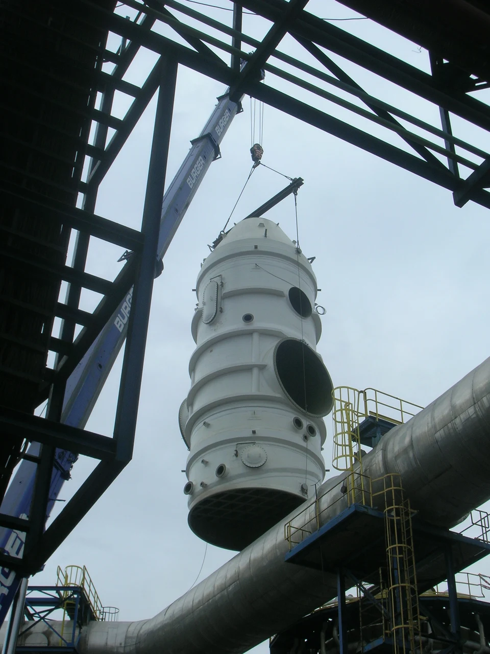 Industrial equipment being installed by crane at a plant.