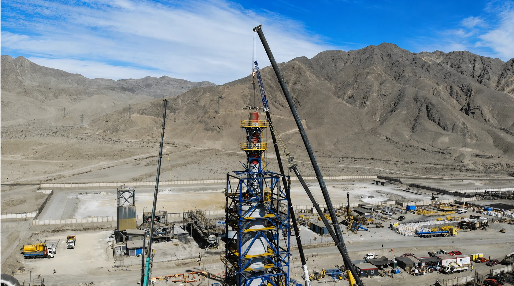 General view of the desulfurization tower assembly site, with cranes next to the structure and mountains in the background.