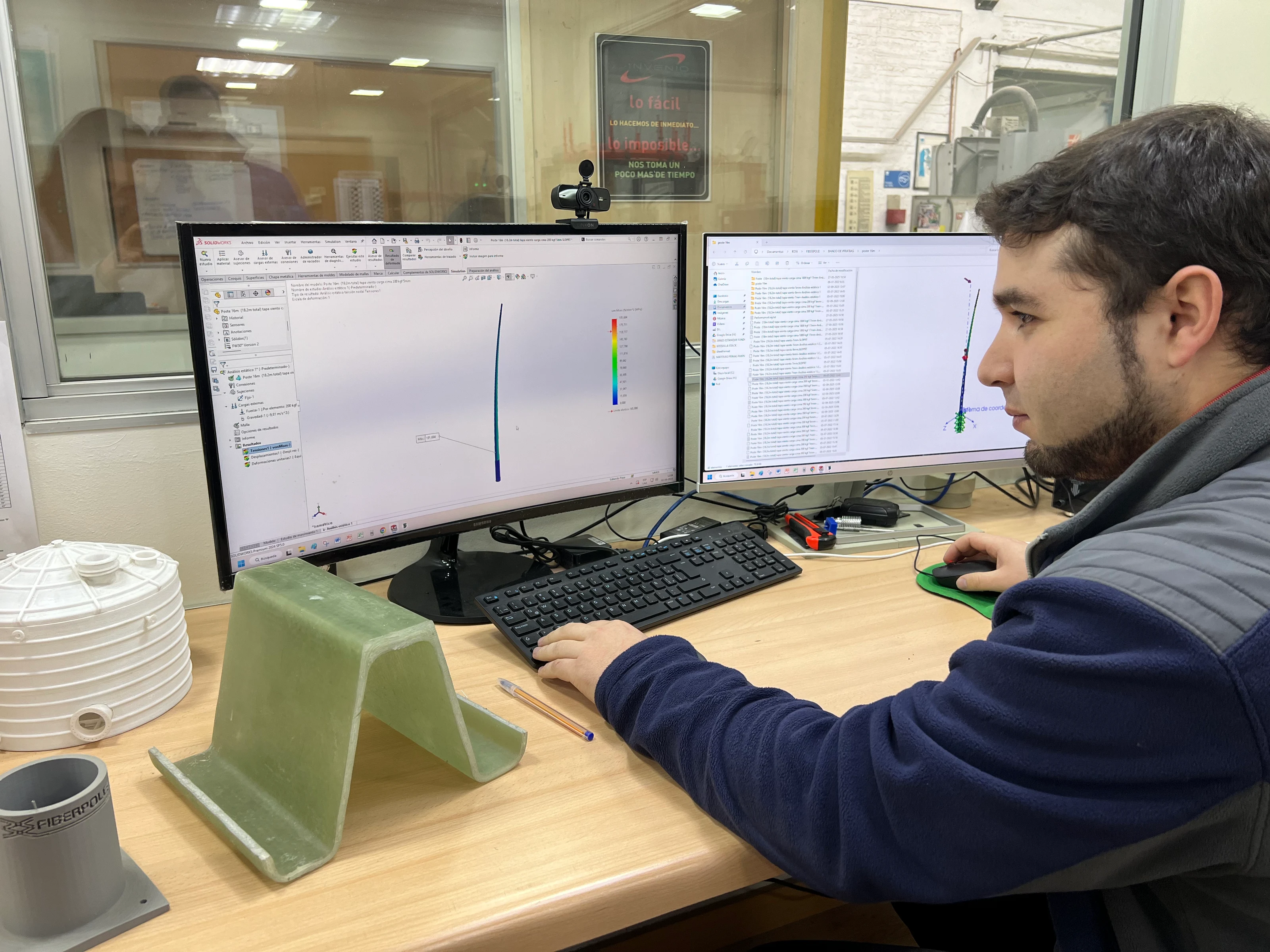 Engineer at a workstation with a structural simulation model on screen and an FRP laminate test coupon on the desk.
