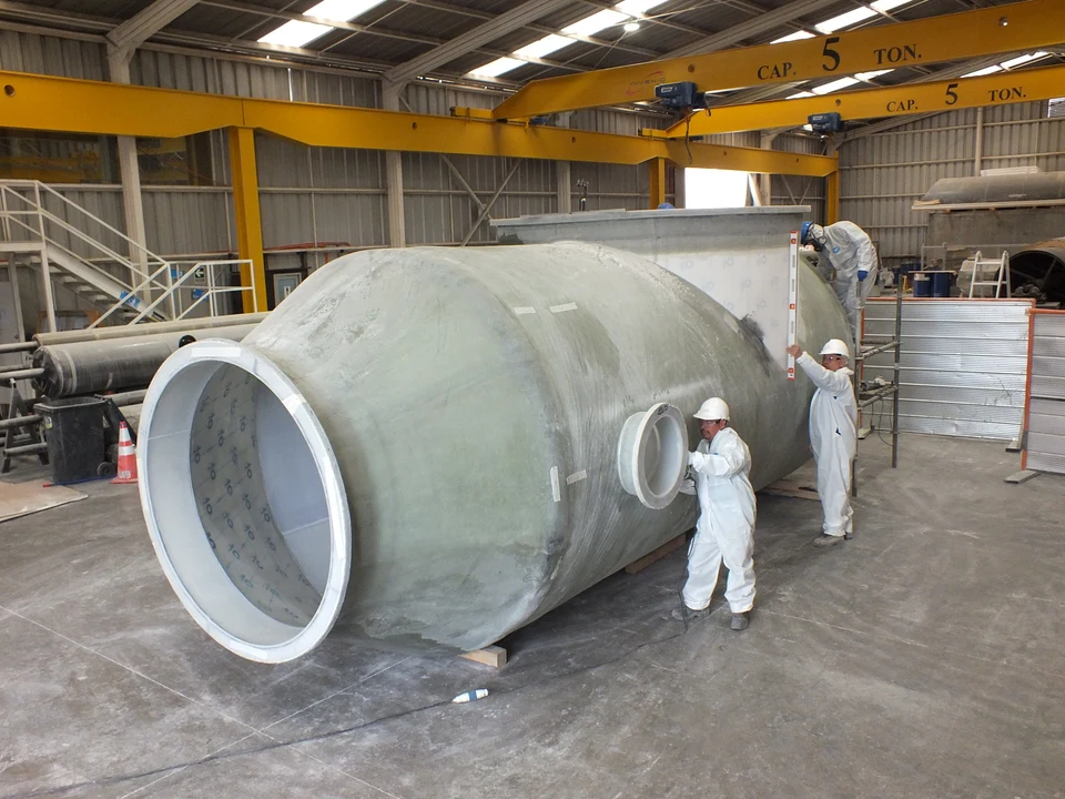 Workers leveling and positioning nozzles on a large-format FRP tank inside the plant.