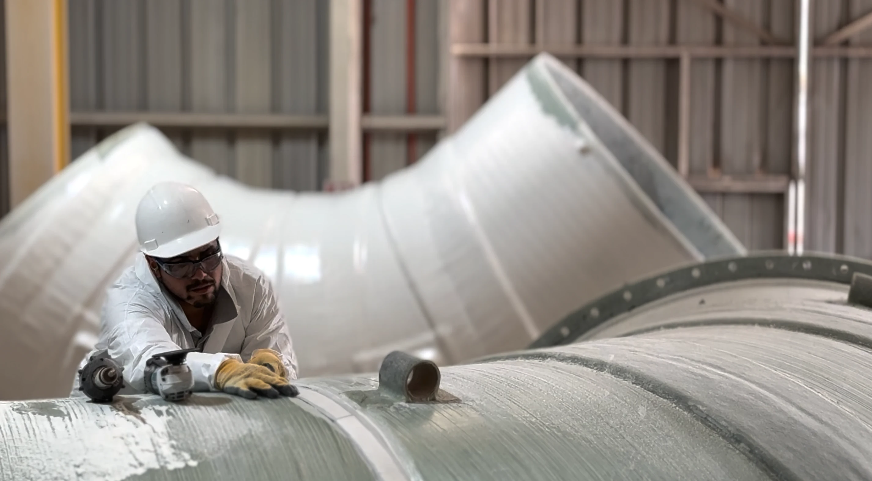 Worker with helmet and gloves using a grinder on the surface of a large-diameter FRP elbow.