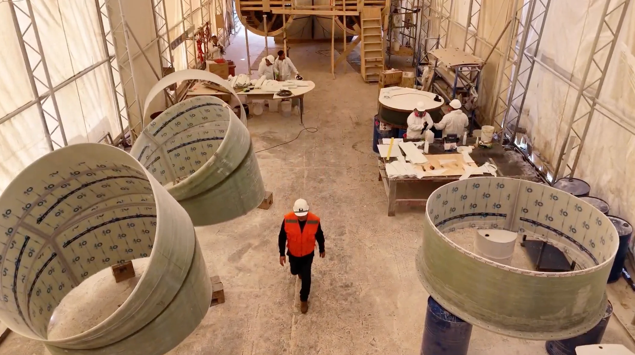 Overhead view of the lamination hall, with large-diameter FRP duct sections and workers among them.