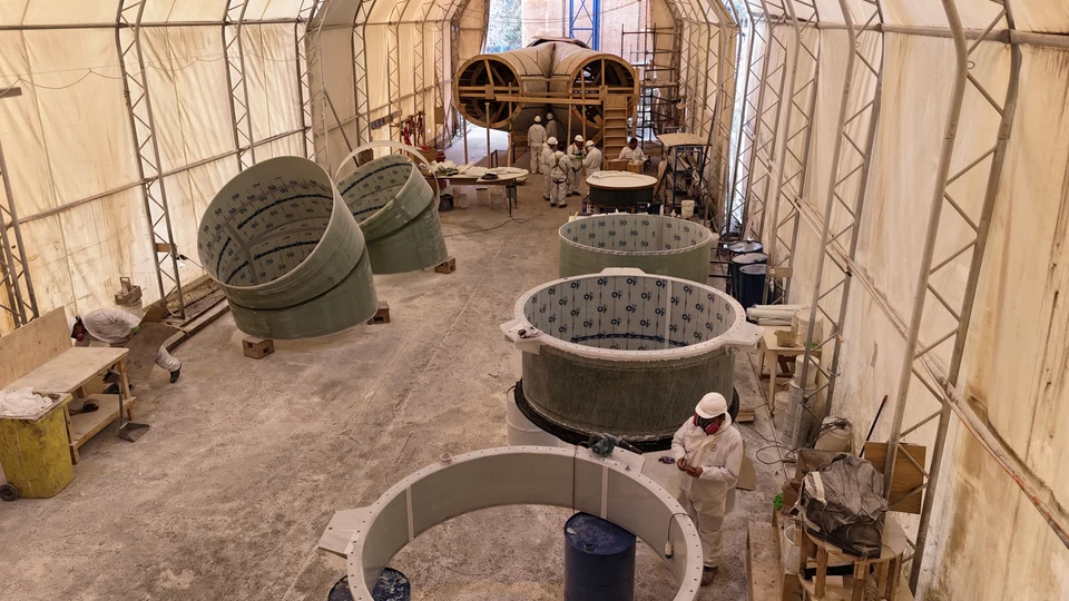 Interior view of the lamination hall, with large-diameter FRP duct sections at different stages and workers among them.