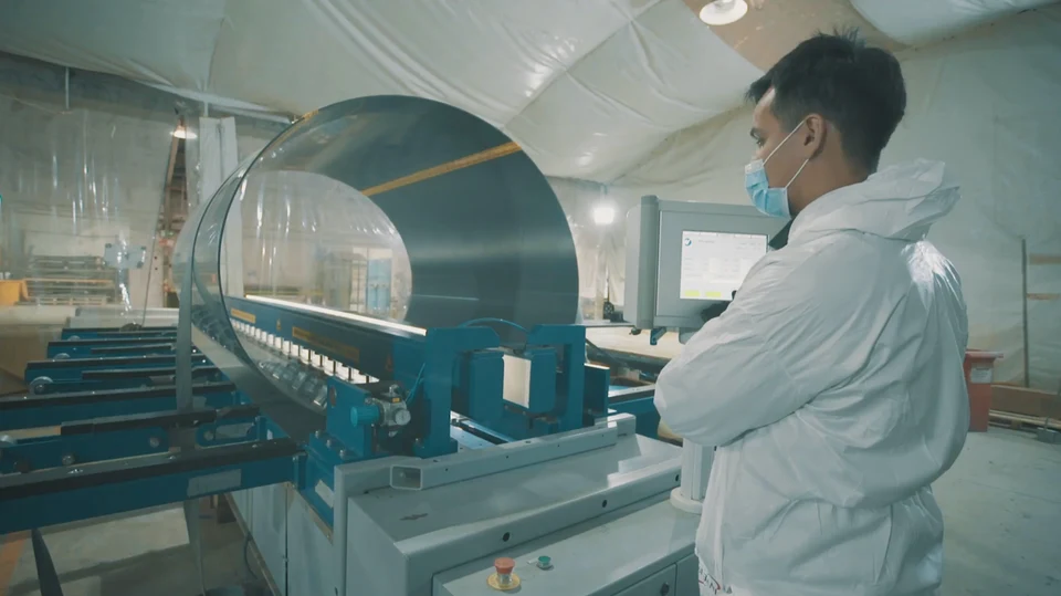 Operator next to a filament winding machine while it winds fiber onto a cylindrical mandrel.