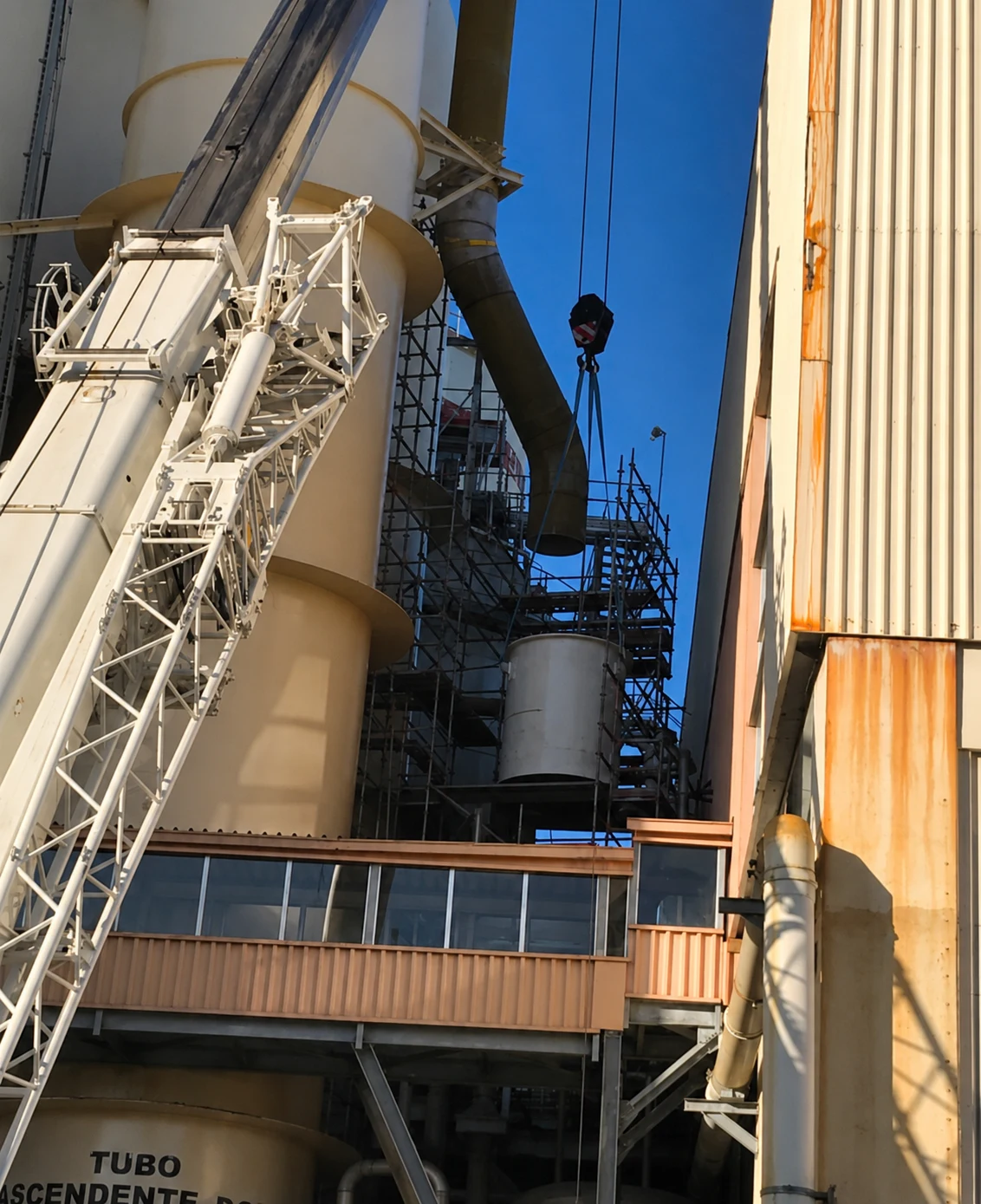 Crane lifting a cylindrical section of the new scrubber between scaffolding, against a clear sky.