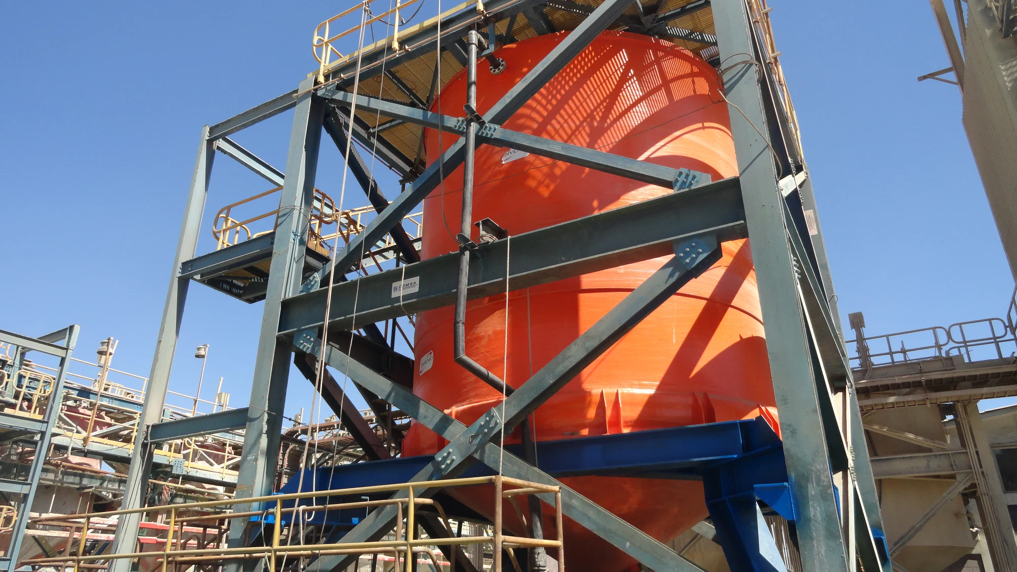 Crane lifting a cylindrical FRP component next to the scaffolding of the desulfurization tower, in an industrial facility.